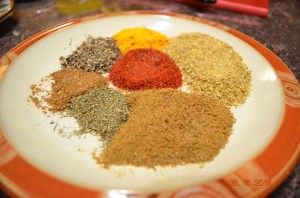 Clockwise from the top: turmeric, coriander, cumin, methi, garam masala, black pepper. Center: chili powder
